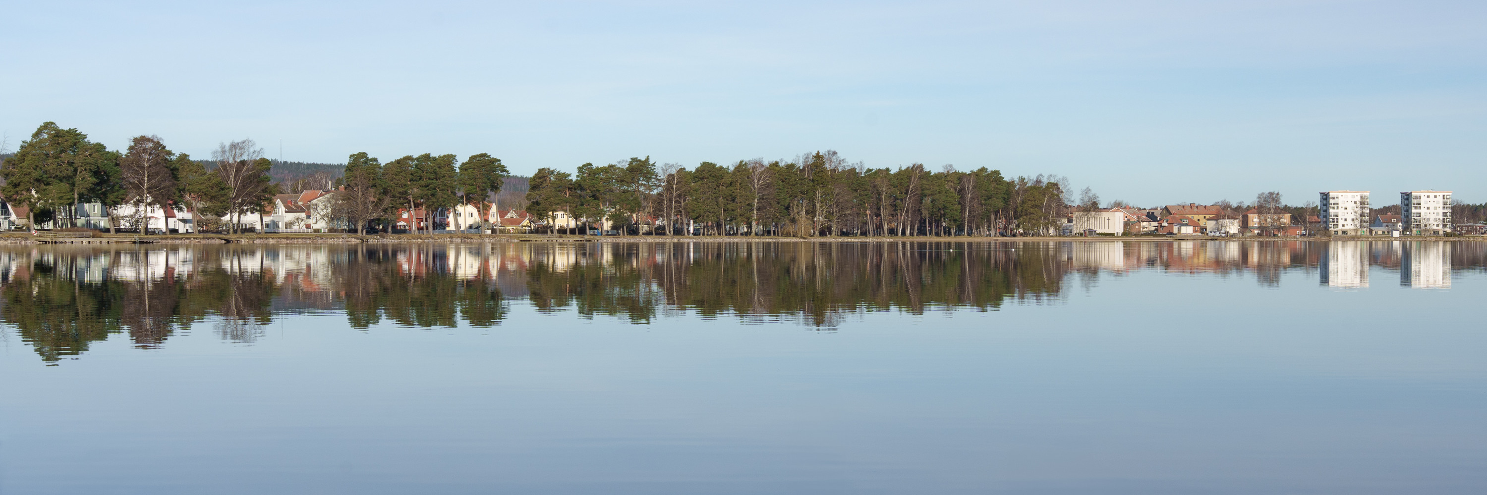 Vy över Vättern med träd och byggnader i bakgrunden.