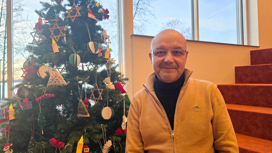 En man står inomhus framför en julgran.