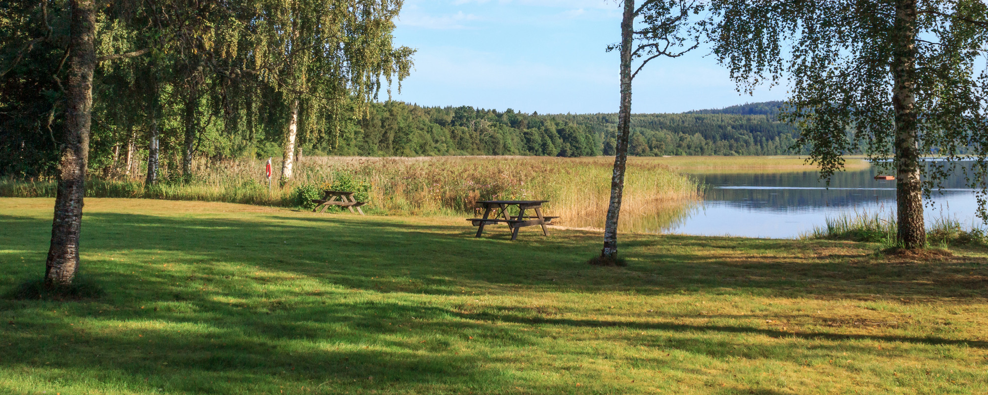 Ett picknickbord mitt på en gräsplätt intill en sjö