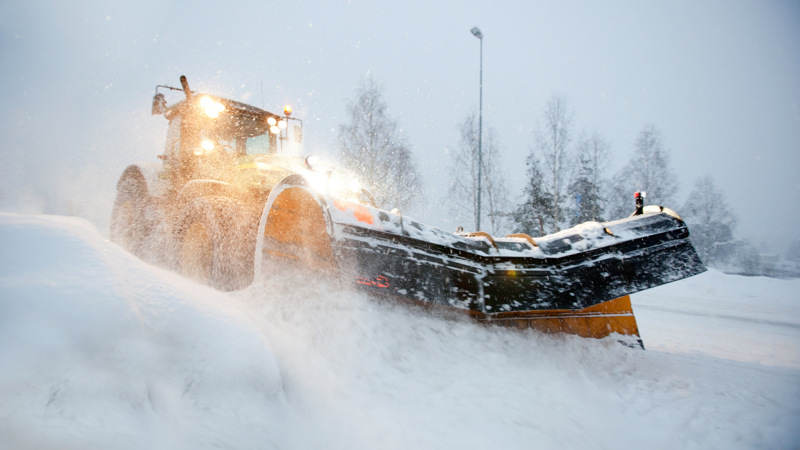 En hjullastare som plogar snö i ymnigt snöfall. Det ligger mycket snö på marken. 