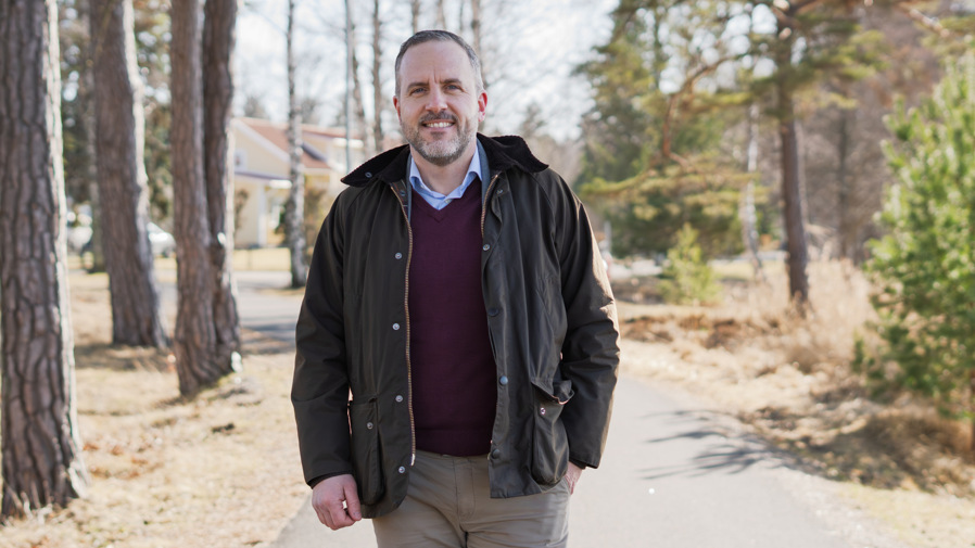 Kommundirektör Johan Myhrman står leendes på en gångväg med natur runt omkring sig.