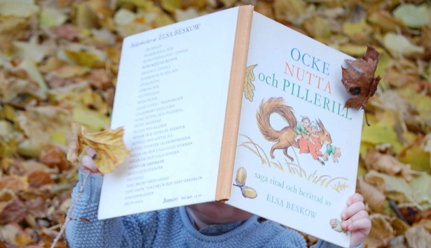 Barn i höstlöv med en bok