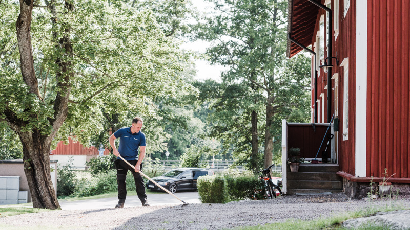 Vaktmästare krattar grusgång.