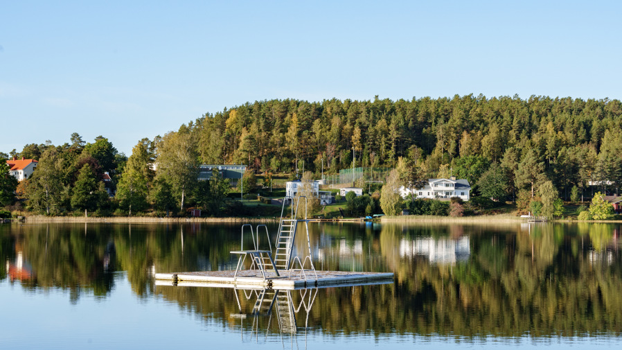 Ett hopptorn på flotte i vattnet med träd och hus i bakgrunden