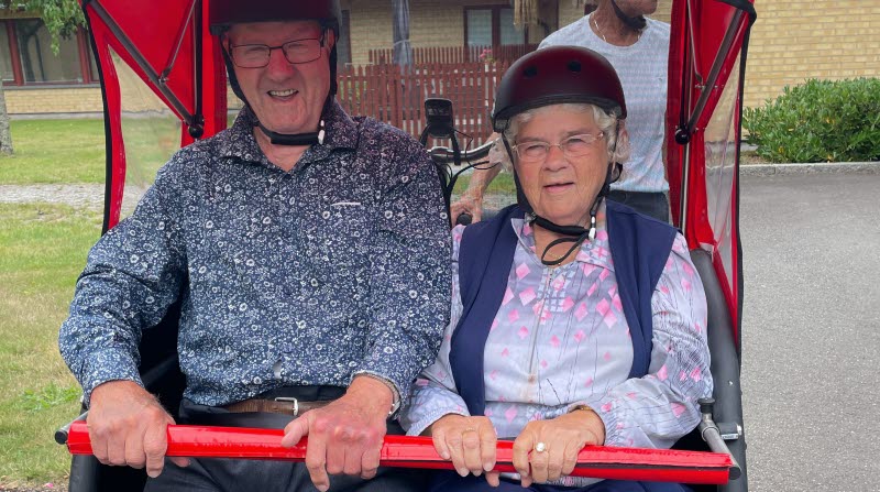 Två äldre personer sitter i en rikshaw 