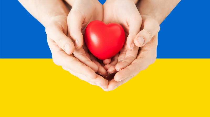 Händer som håller i ett rött hjärta med Ukrainas färger i bakgrunden