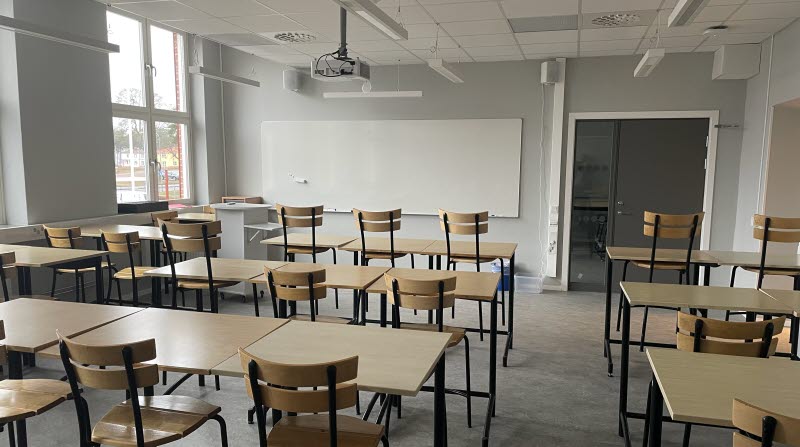 Klassrum med bänkar och stolar i bakgrunde finns whiteboardtavla och dörr in till anslutande grupprum