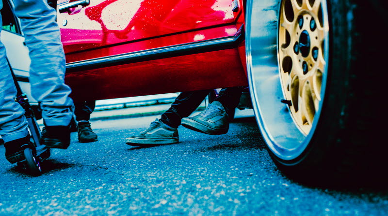 Fälg på en röd bil och ungdomar vars skor endast syns. 