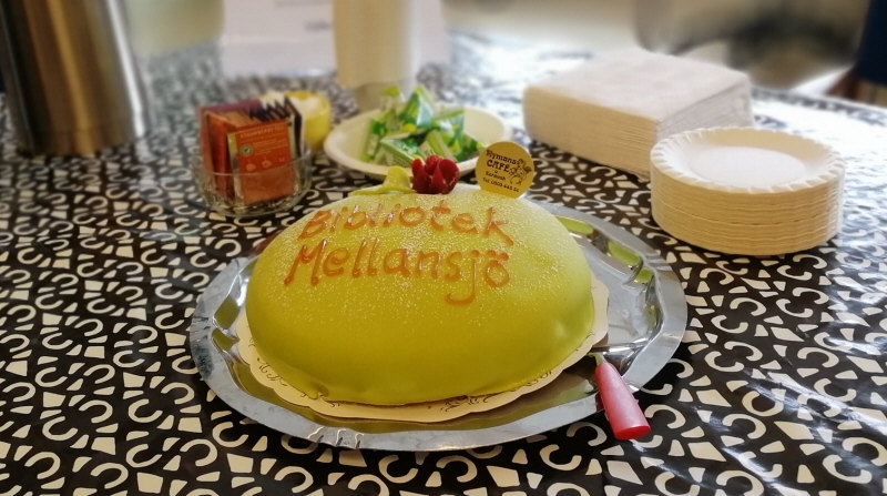 Grönprinsesstårta med texten Bibliotek Mellansjö. Uppdukat bord med tallrikar, termosar och liknande.