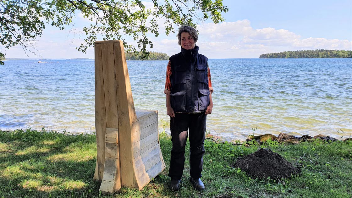 Konstnären Katarina Vallbo bredvid skulpturen & konstverket "viska, lyssna", som föreställer en stol. Verket står vid Vätterns strandkant.